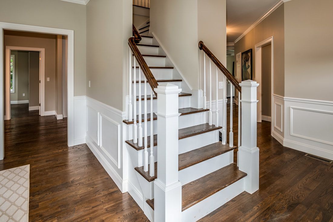 A white staircase with wooden steps and a wooden railing in a hallway.