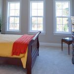 A bedroom with a bed , dresser , fireplace and many windows.