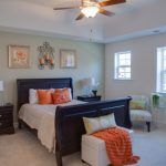 A bedroom with a bed , chair , nightstand and ceiling fan.