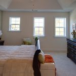 A bedroom with a bed , dresser , chair and windows.