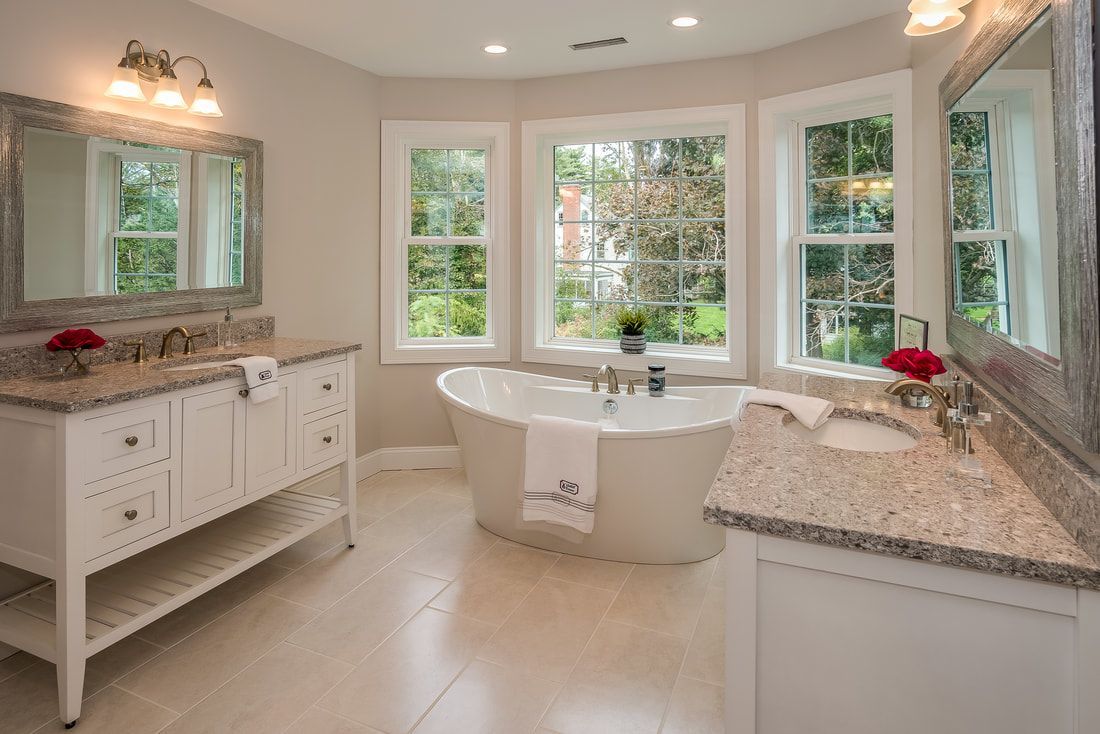 A bathroom with a tub , sinks , mirrors and two windows.