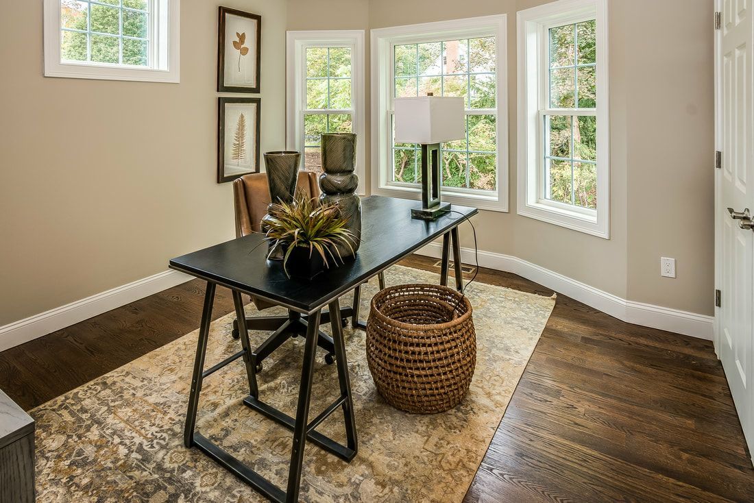 A home office with a desk , chairs , a lamp and a rug.