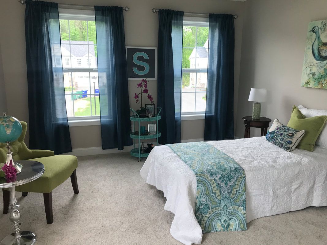 A bedroom with a bed , chair , table and two windows.