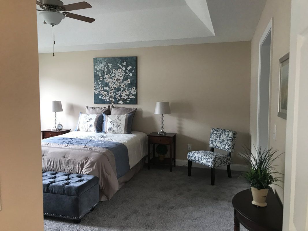 A bedroom with a bed , chairs , lamps and a ceiling fan.