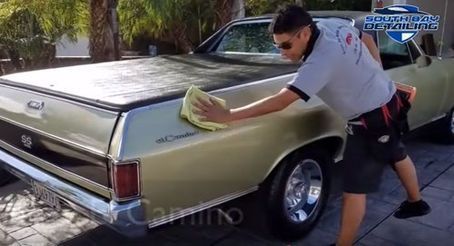 A man is cleaning a car with a towel.