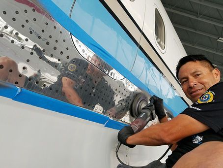 A man is polishing the side of an airplane with a grinder.
