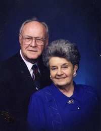 Elderly couple posed together in formal attire against a dark blue studio backdrop
