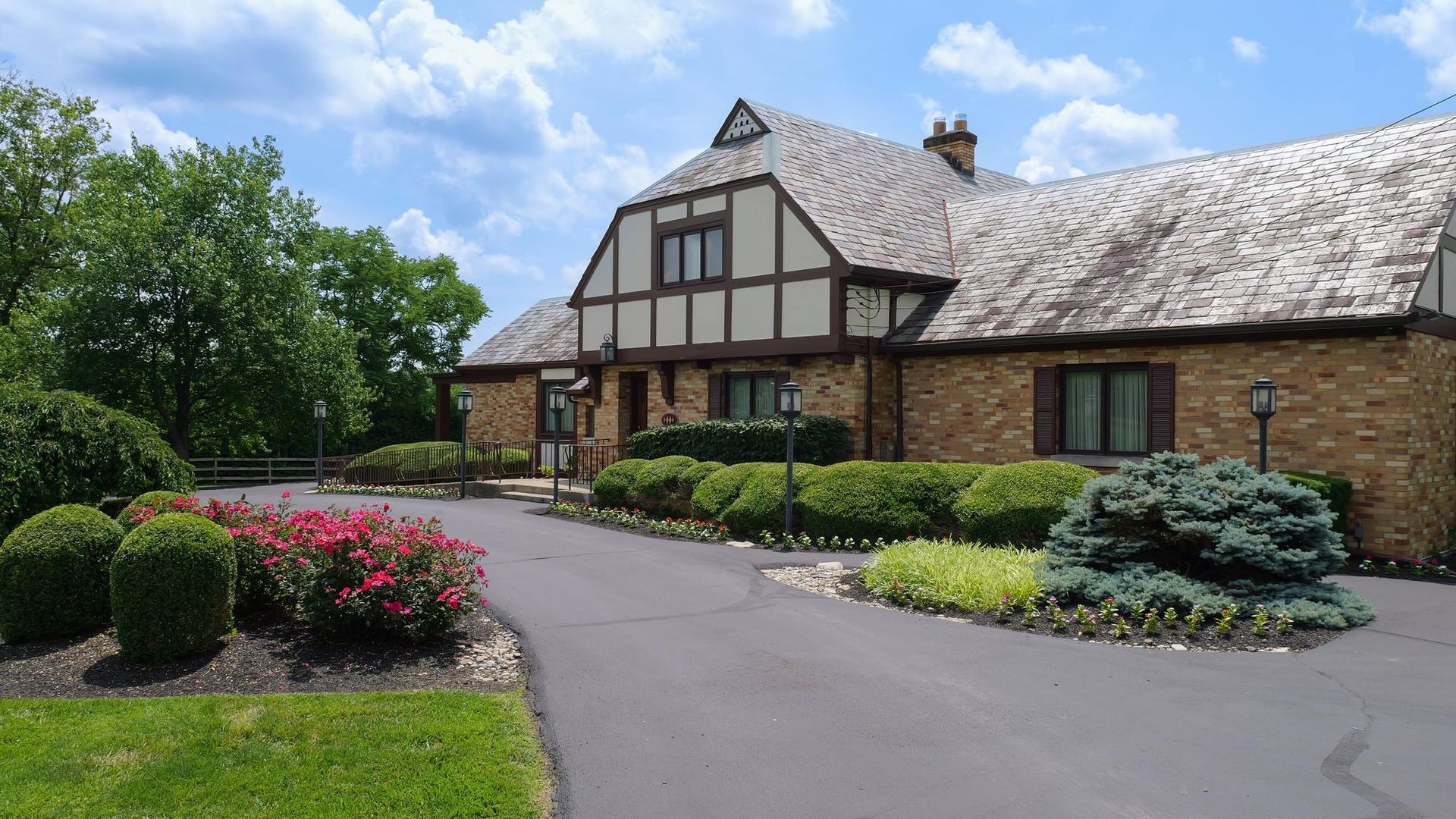 Tudor-style brick building with a thatched roof, surrounded by landscaped gardens and a curved driveway