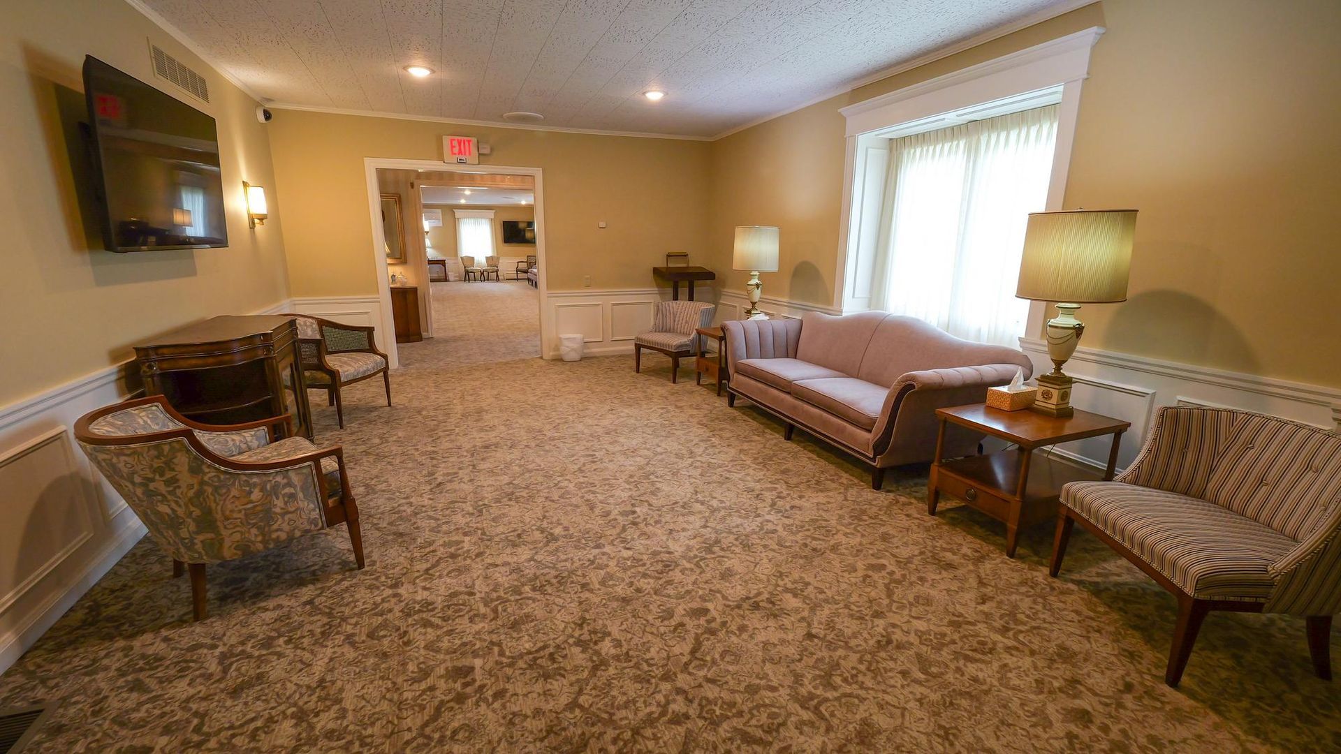 Spacious beige living room with sofas, chairs, lamps, and a fireplace under soft window light