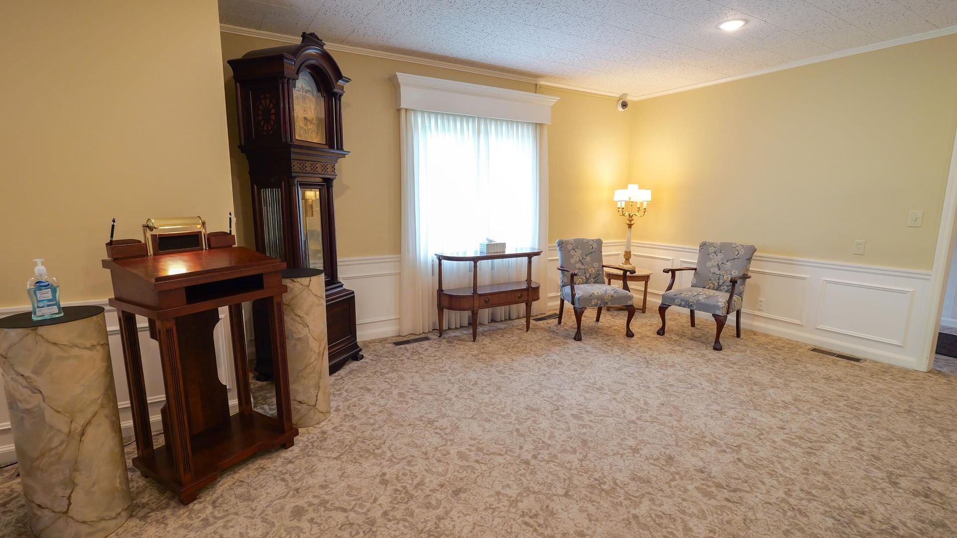 Living room with carpet, fireplace, grandfather clock, window, and seating by a lamp