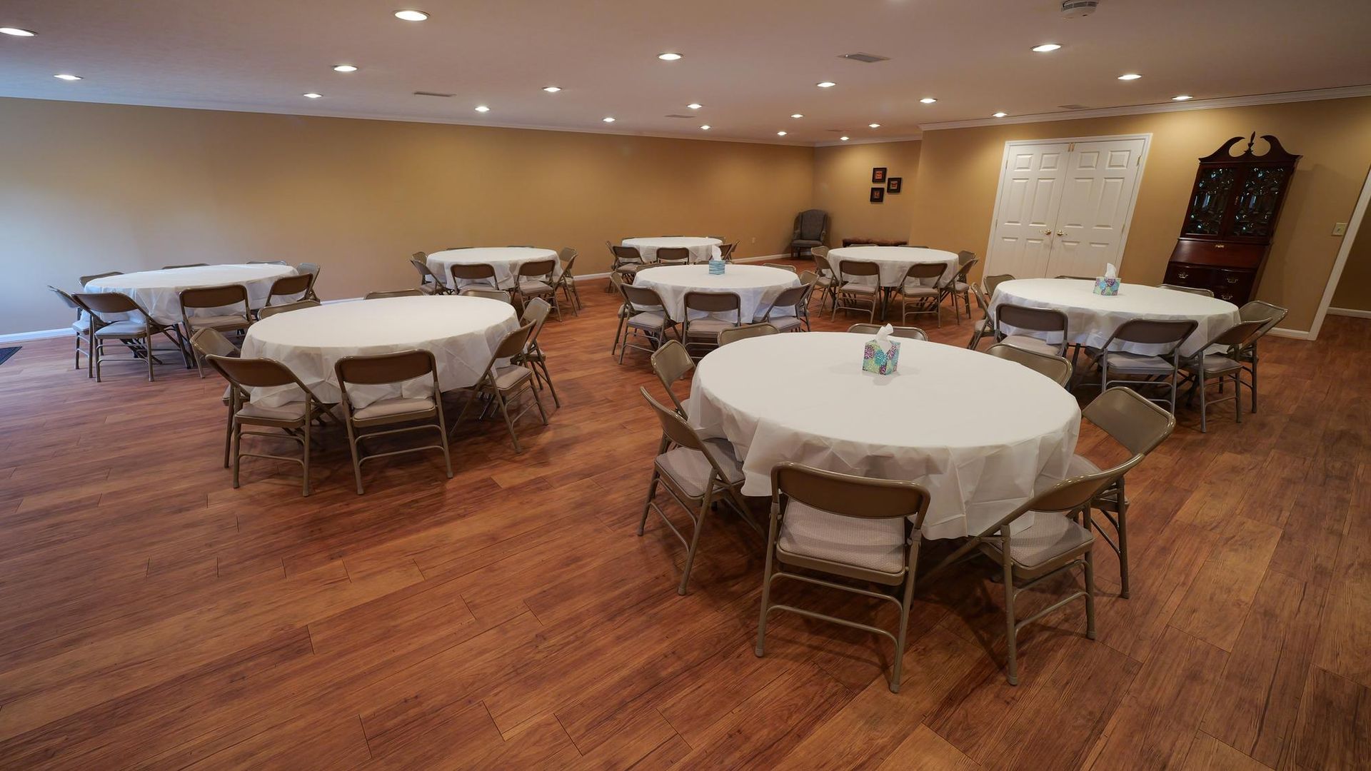 Empty banquet room with round tables, white tablecloths, and wooden chairs on a polished floor.