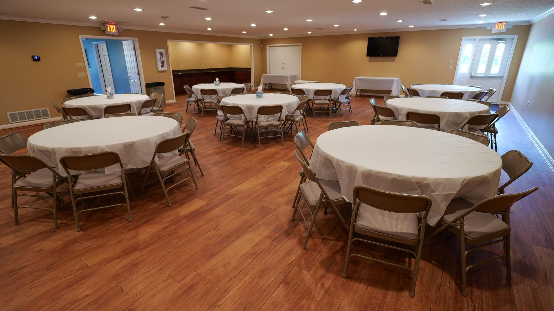 Empty banquet hall with round tables covered in white tablecloths and folded chairs on wood floors