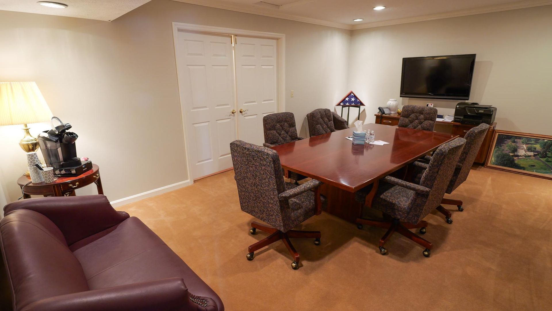 Conference room with wood table, swivel chairs, couch, TV, and lamp under recessed lighting