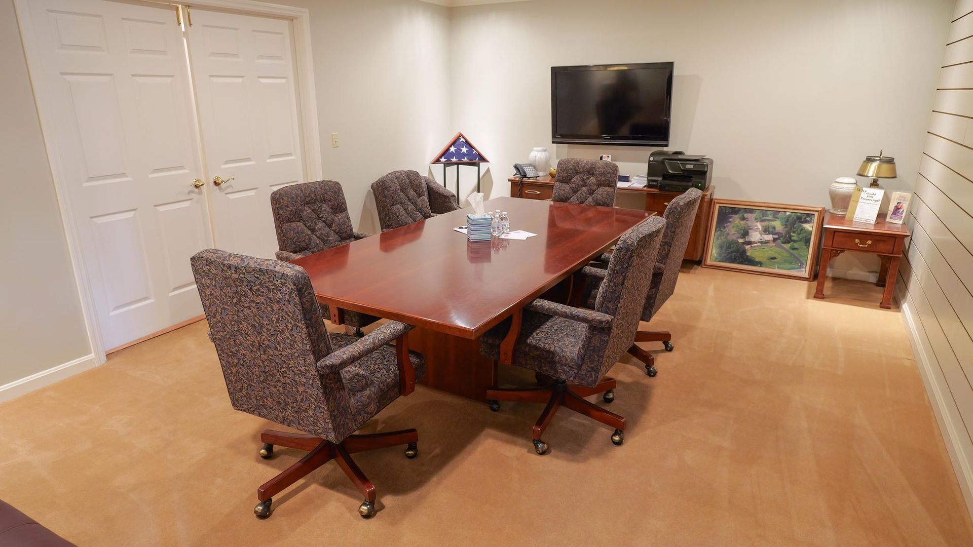 Conference room with a wooden table, patterned chairs, TV, and closed white double doors.