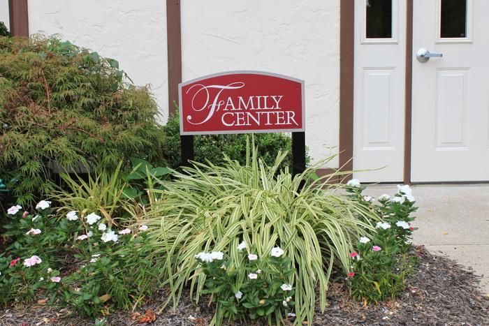 Red Family Center sign beside a white door, with shrubs and flowers in front of a building.