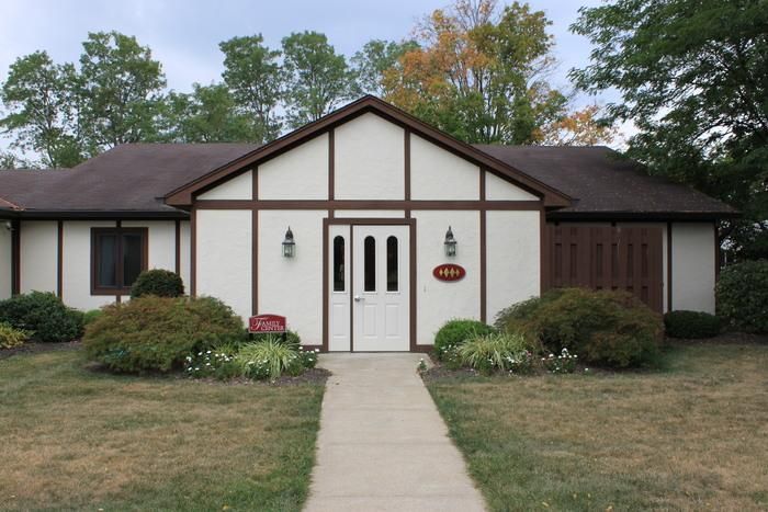 Single-story house with white front doors, brown roof, and a walkway leading to the entrance.