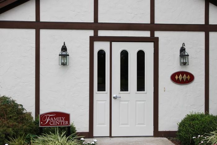 White double doors on a building with red trim, flanked by wall lanterns and small signs.