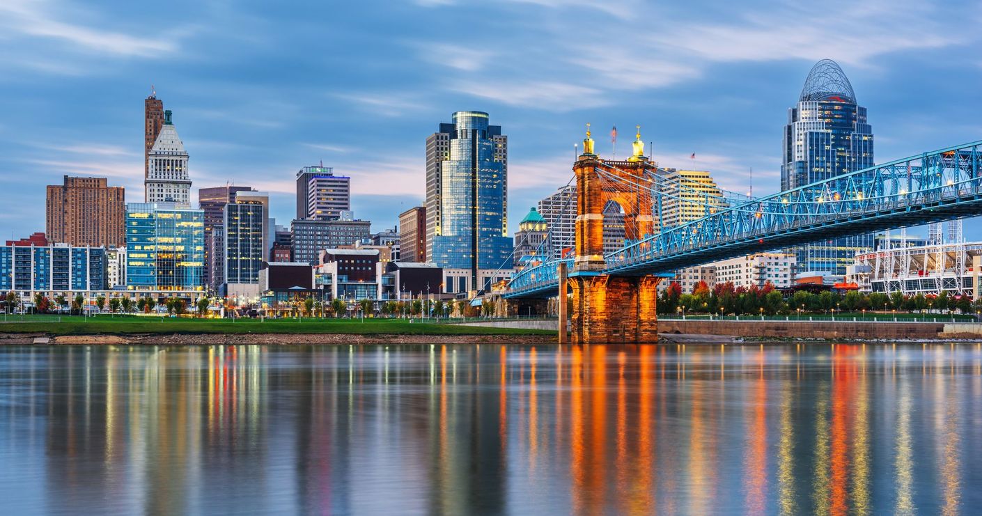 Cincinnati skyline at dusk with a lit suspension bridge reflecting on the river