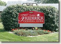 Frederick Funeral Home sign on red plaque amid trimmed hedges and flowers