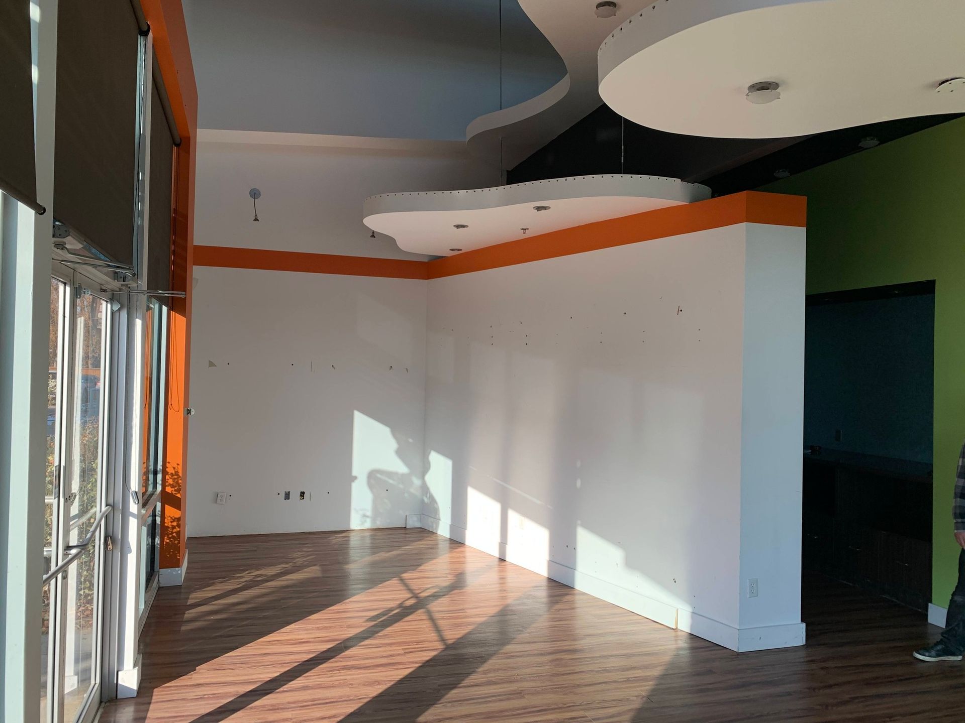 Empty modern room with white walls, wood floor, orange accent trim, and large windows casting sunlight shadows