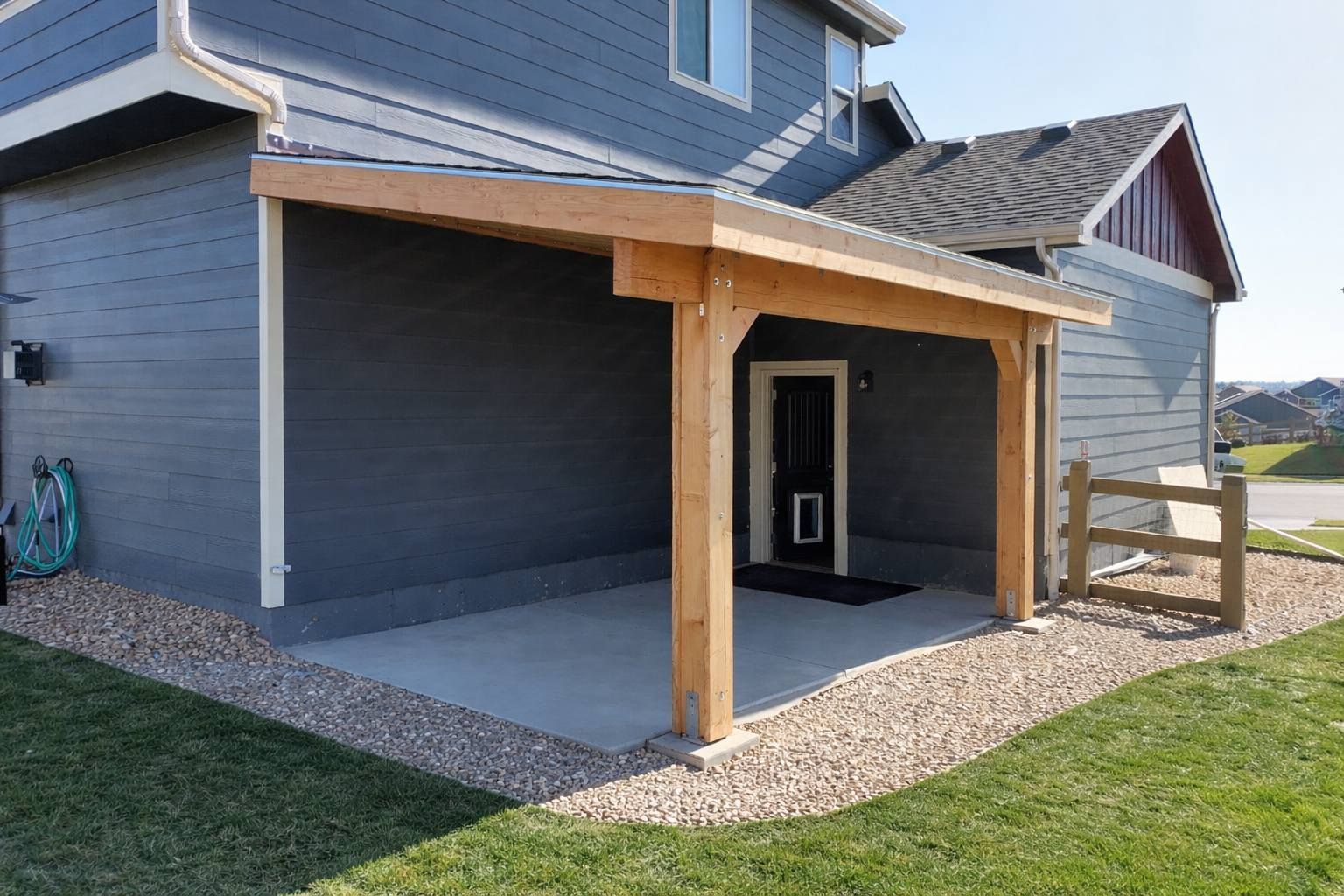 Covered front porch with wooden posts on a gray house and a small gravel patio beside a lawn