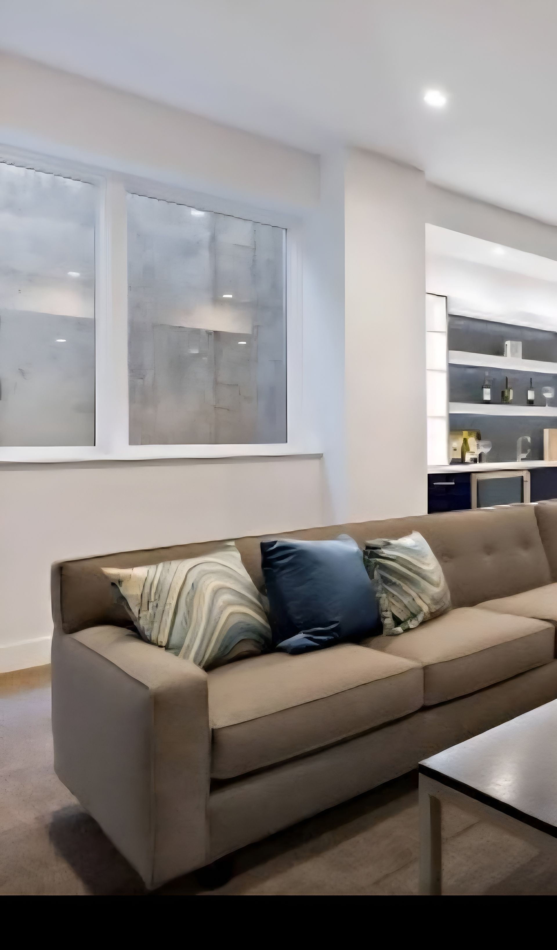 Modern living room with beige sectional sofa, patterned pillows, coffee table, and large window.