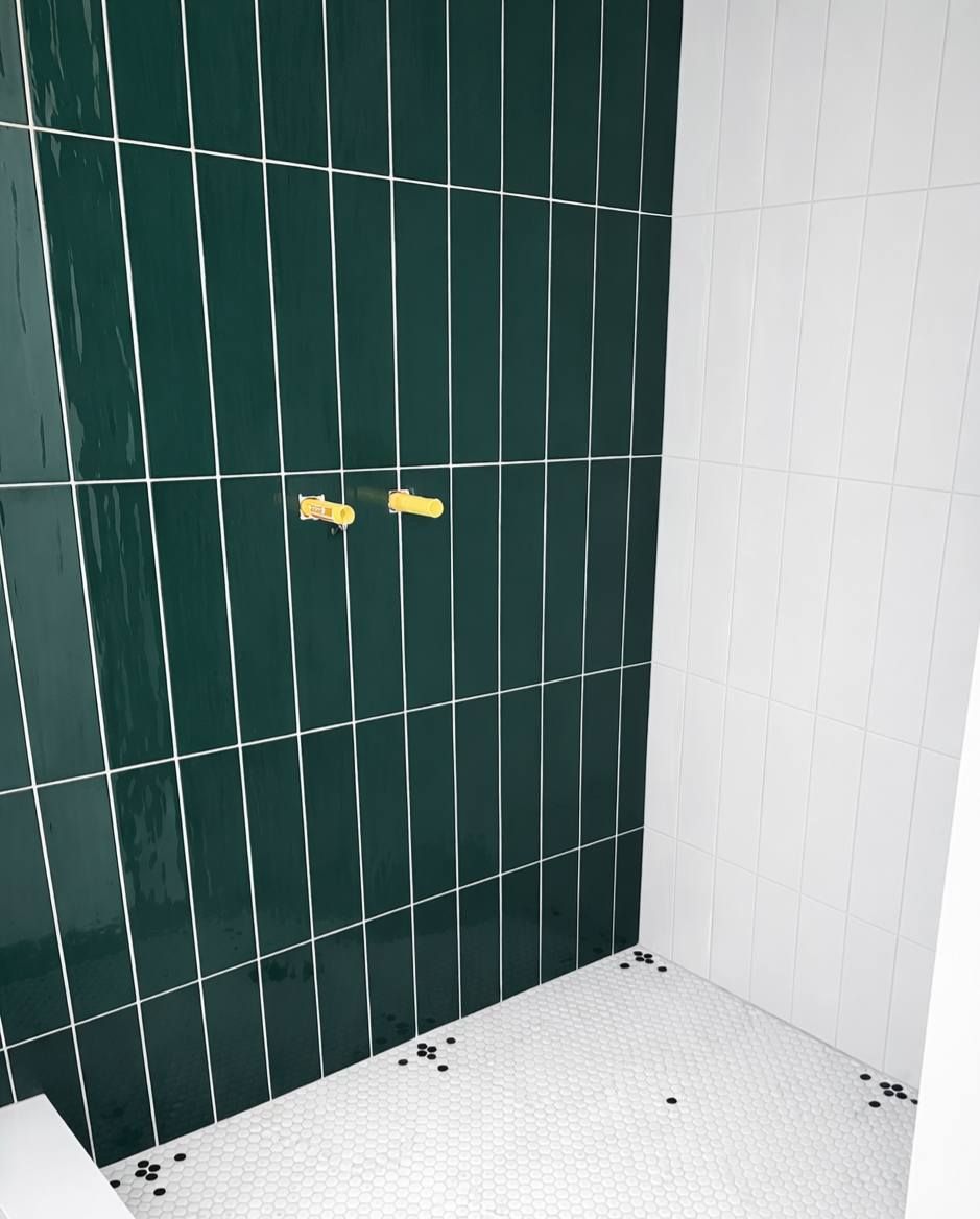 Tiled shower corner with dark green and white wall tiles and two yellow wall fixtures