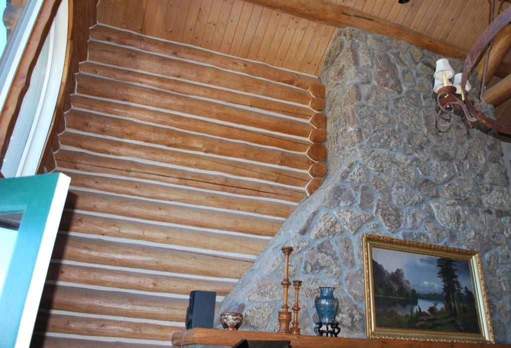 Log cabin interior with log wall, stone fireplace, and framed landscape painting on a mantel