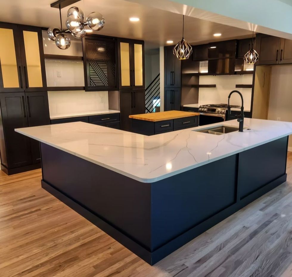 Modern kitchen with large white island, dark cabinets, wood floors, and pendant lights