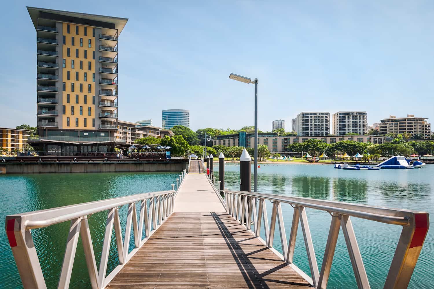 A Dock Leading to a Body of Water With a Tall Building — John Day Plumbing in Darwin, NT