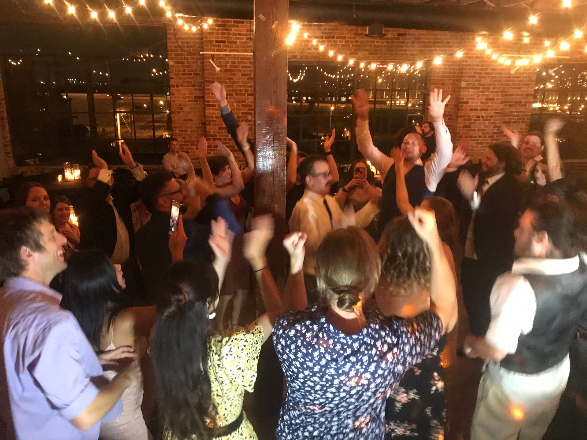 People dancing with raised hands at a warmly lit indoor party under string lights