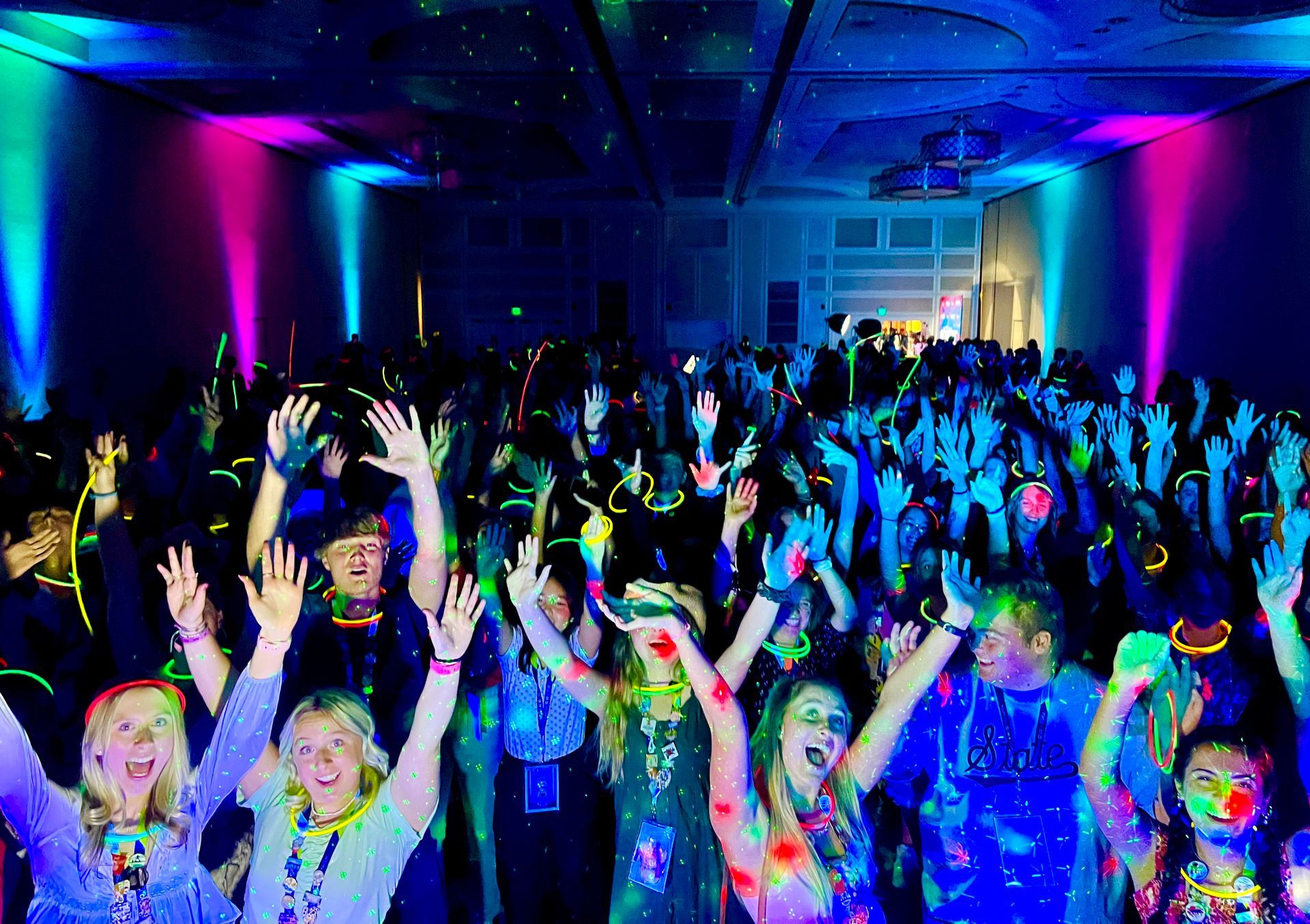 Crowded dance floor at a party, with people raising hands under bright blue and pink lights