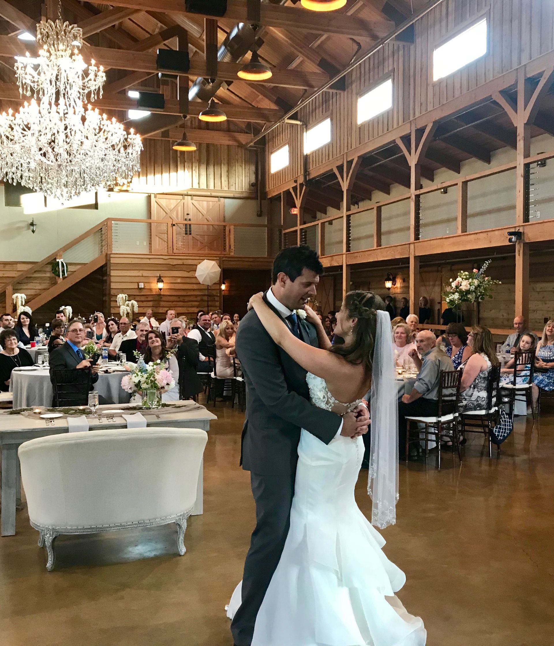 Bride and groom dancing in a rustic barn reception with guests seated nearby