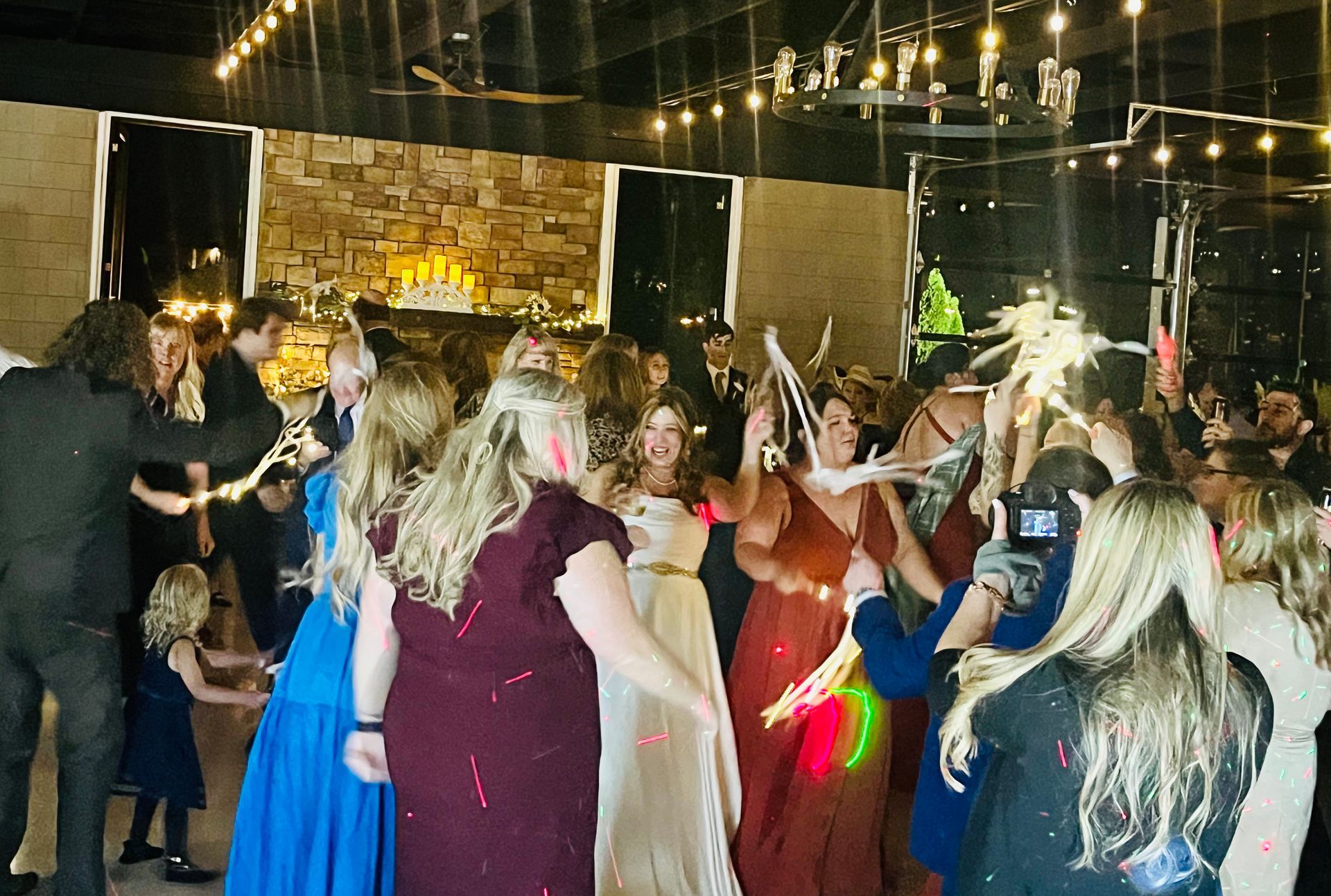 People dancing at a lively indoor party with string lights and a stone wall backdrop