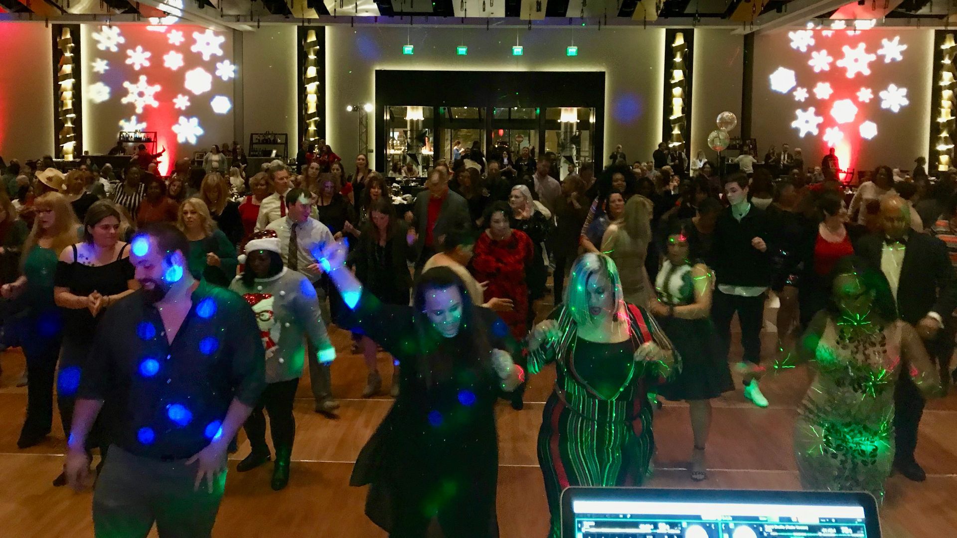 Group dancing in a hall, with colorful holiday lights and decorations, under glowing red and green snowflakes.