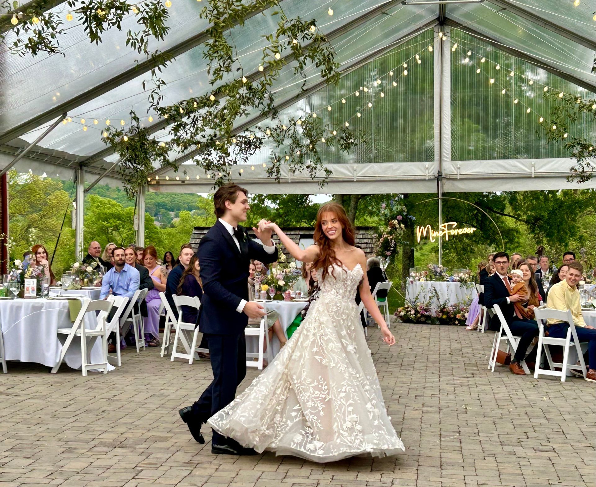 Bride and groom dancing at an outdoor wedding reception under a glass pavilion