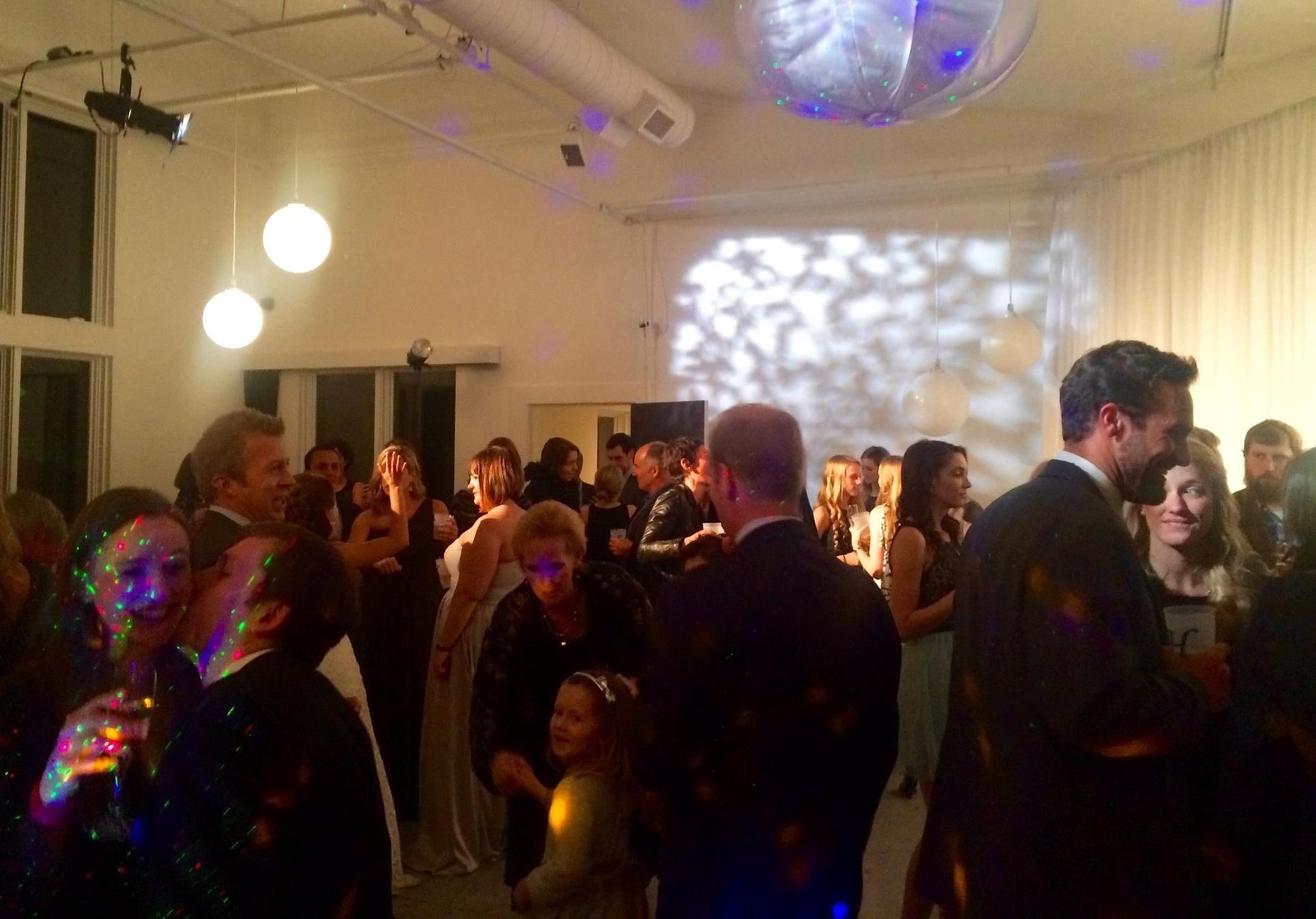 A group of people at a dimly lit indoor event with decorative lighting, mingling and socializing in a party setting.