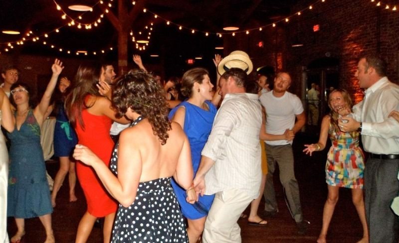 A group of people dancing in a dimly lit, rustic venue decorated with string lights.