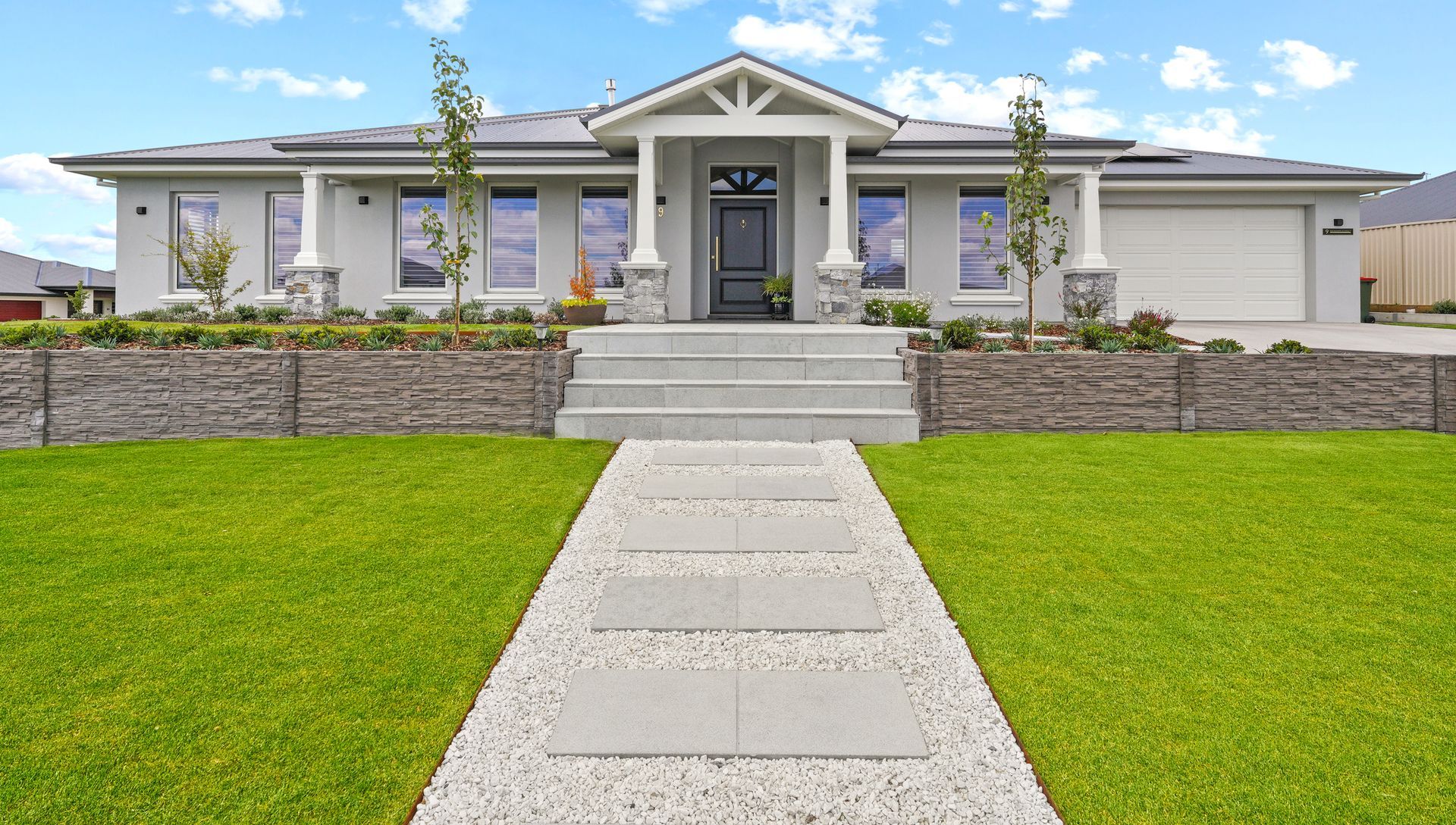 Modern residential landscape construction featuring a paved entrance, garden beds, concrete sleeper retaining wall and turf
