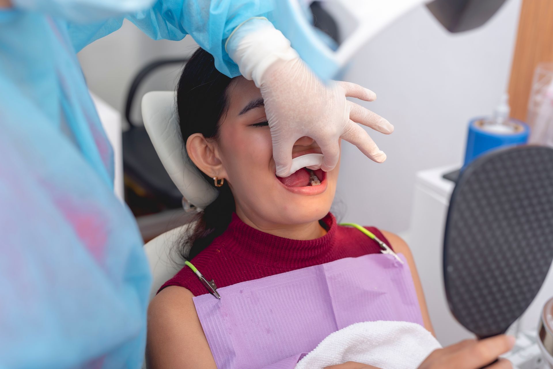 Dentist examining a patient's mouth with tools in a dental office. The patient is looking in a mirror.