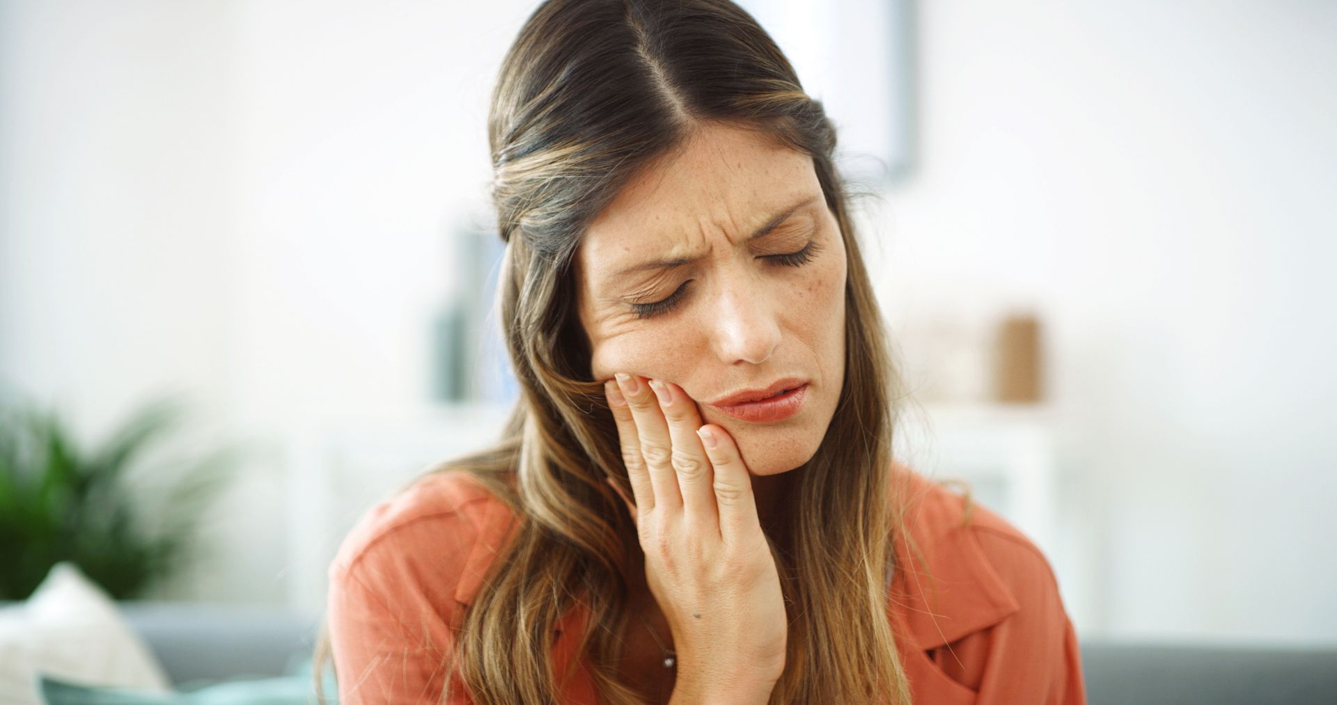 Woman holding her cheek, appearing to be in pain, indoors.