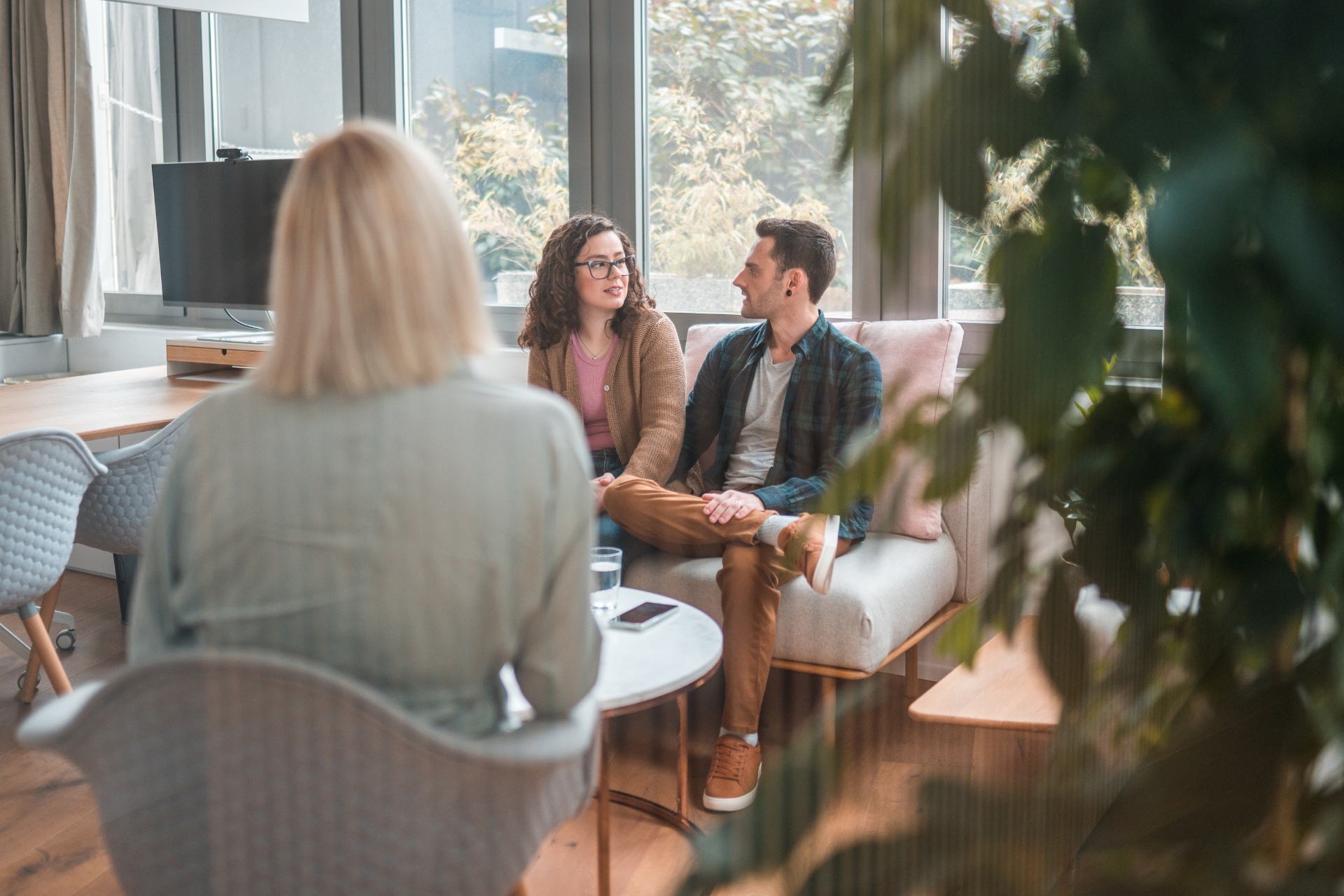 Therapist in light green shirt sits across from couple on couch, discussing relationship.