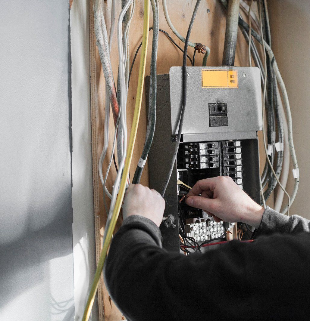 Electrician working on a residential electrical panel, surrounded by wires.