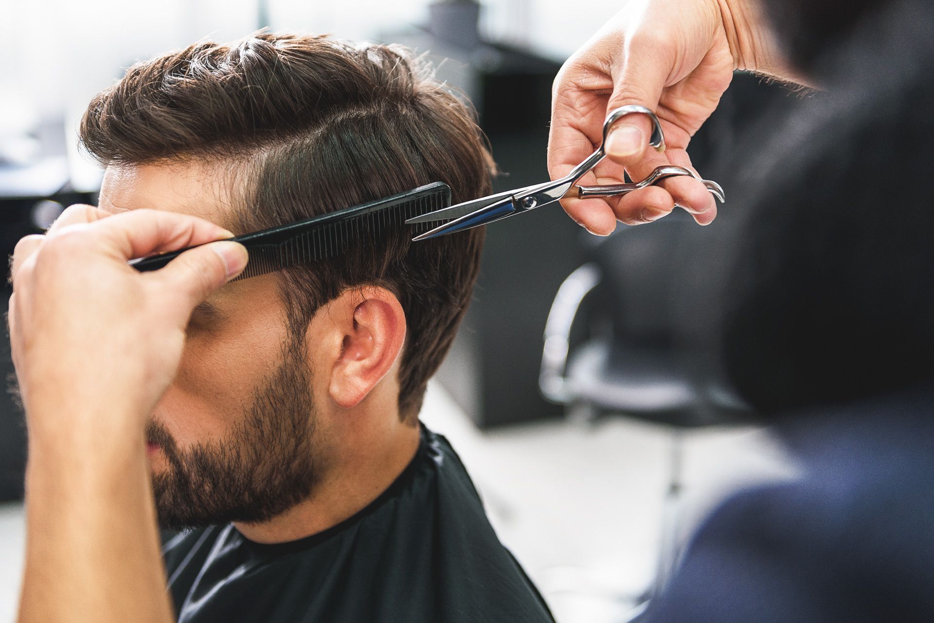 Barbero cortando el cabello oscuro de un hombre con tijeras y peine en un salón.
