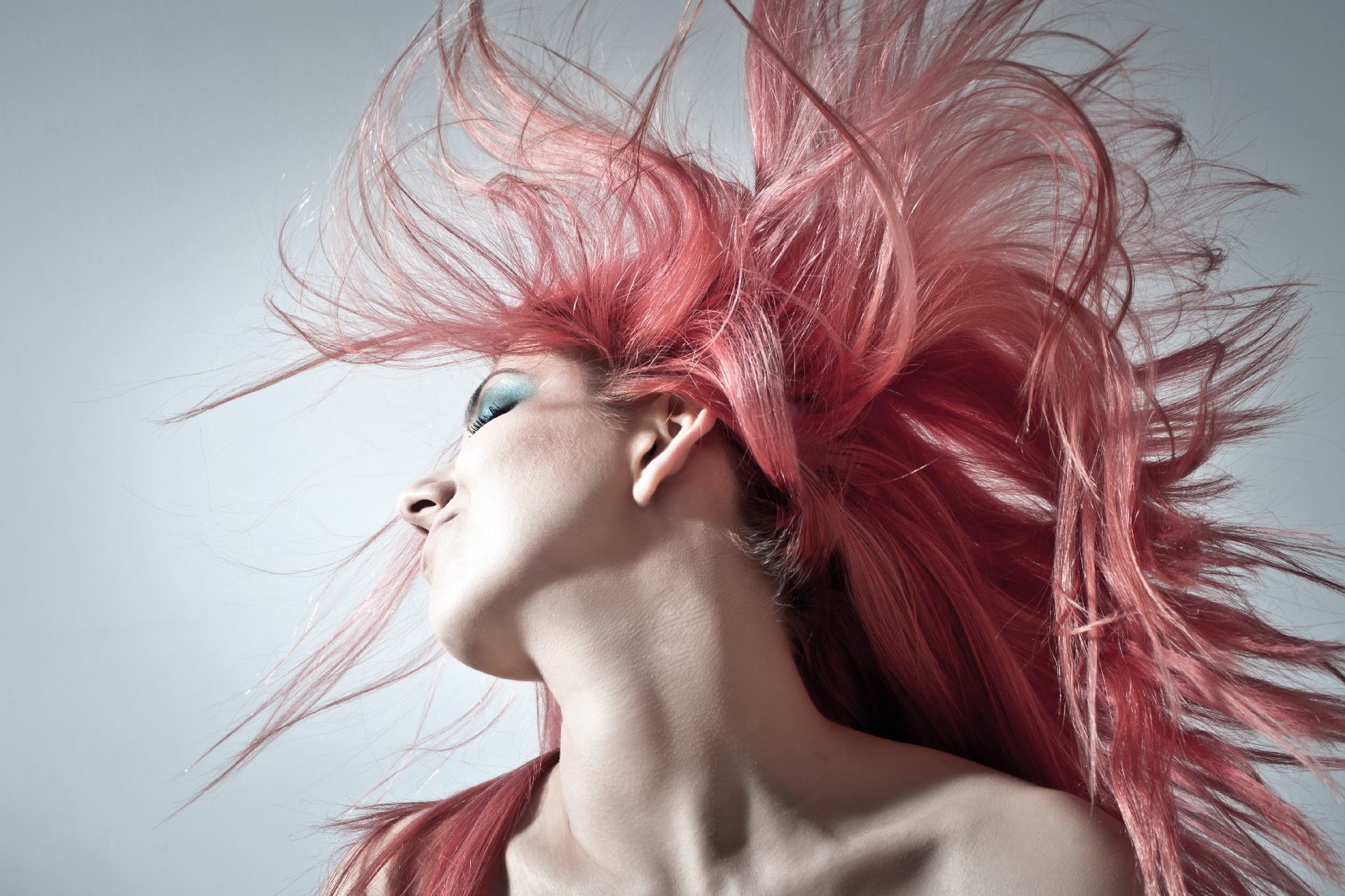 Mujer con cabello rosado al viento mirando hacia arriba, fondo neutro.