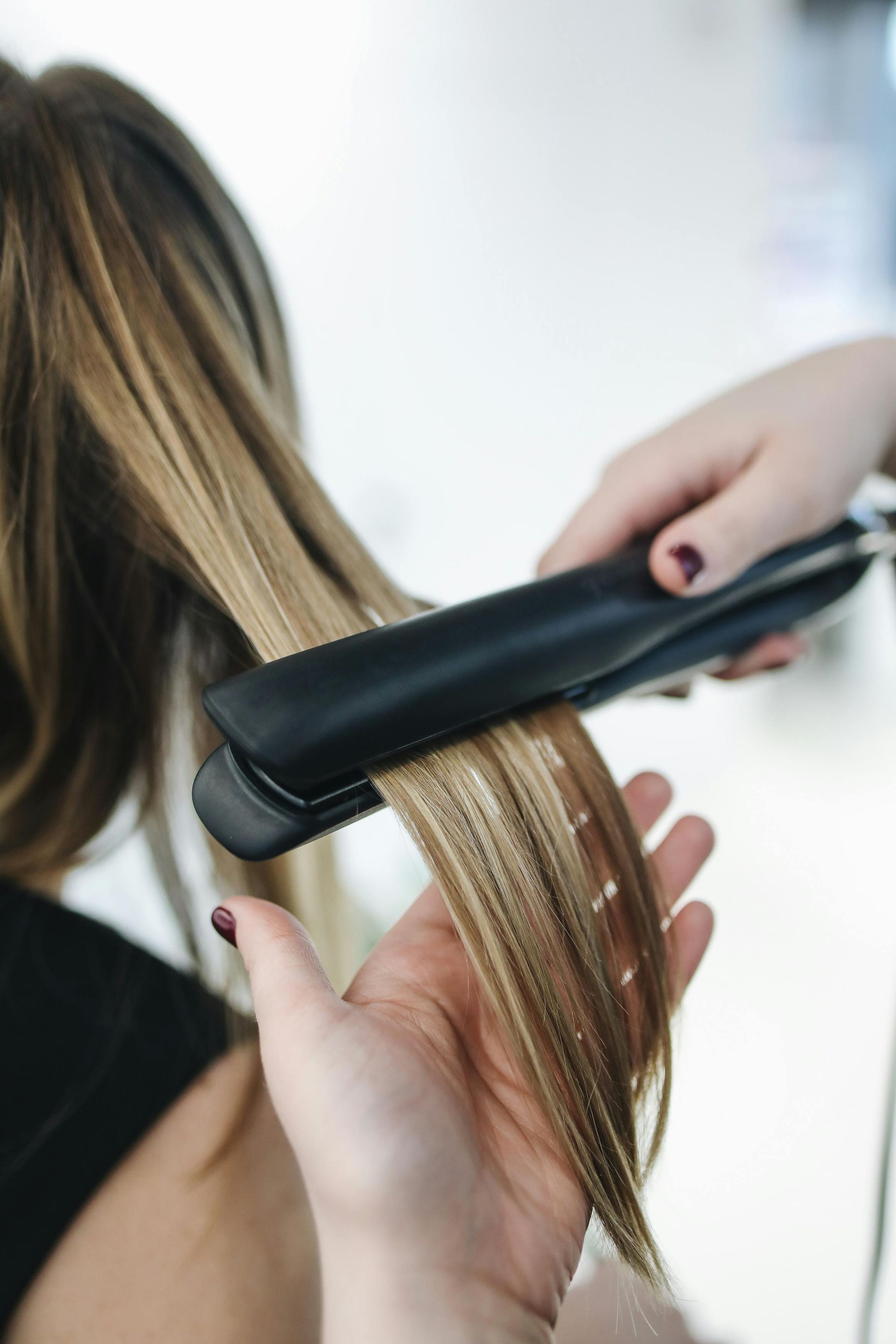 Cabello siendo alisado con una plancha; manos de un estilista sosteniendo el cabello y la plancha en un salón.