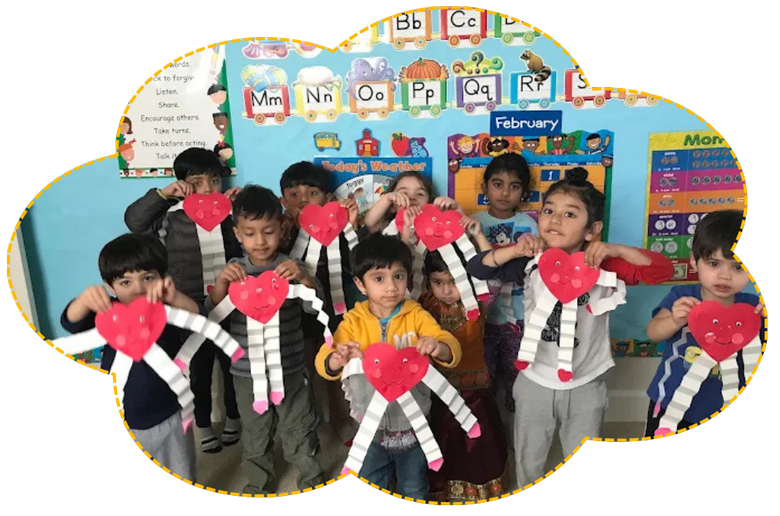 Classroom group of children holding red heart crafts in front of a colorful wall display