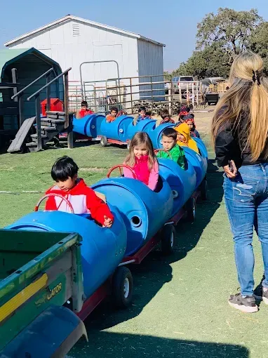 Children riding a blue trackless train at an outdoor fair, with an adult standing nearby