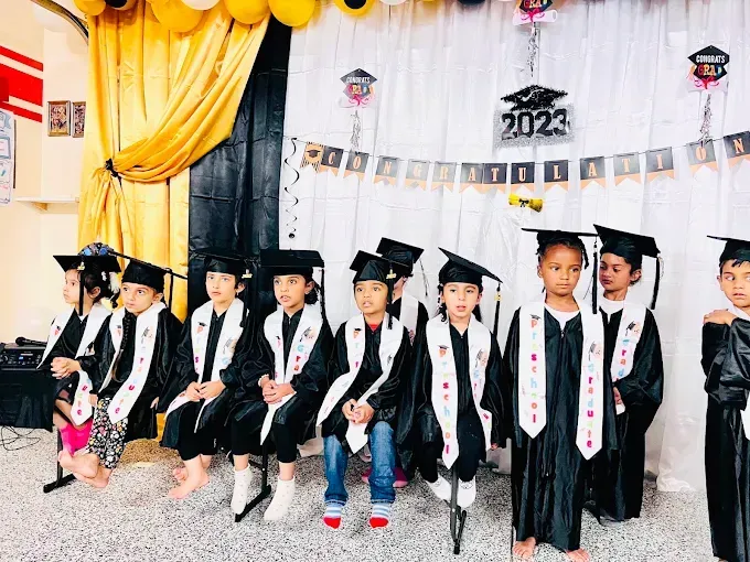 Children in graduation caps and gowns seated on a decorated stage at a 2023 celebration