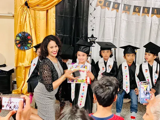 Teacher presenting an award to young graduates in caps and gowns on a decorated stage